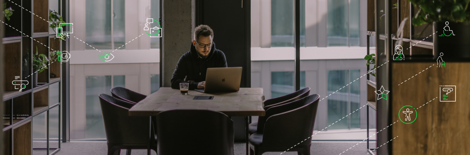 Mężczyzna pracujący przy laptopie, siedzący przy dużym drewnianym stole w nowoczesnym biurze z dużymi oknami. Wokół niego widoczne są ikony związane z technologią, dostępnością, design system, symbolizujące różne aspekty tworzenie dostępnych produktów cyfrowych.Design system a zgodność z WCAG i EAA - Jak design system może wpłynąć na zaangażowania użytkowników a to na realizację celów biznesowych i zwrot z inwestycji.
